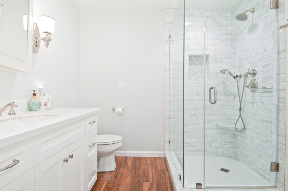 This is an example of a medium sized classic ensuite bathroom in Los Angeles with shaker cabinets, white cabinets, a corner bath, a corner shower, a two-piece toilet, white tiles, metro tiles, white walls, laminate floors, a submerged sink, quartz worktops, brown floors and a hinged door.