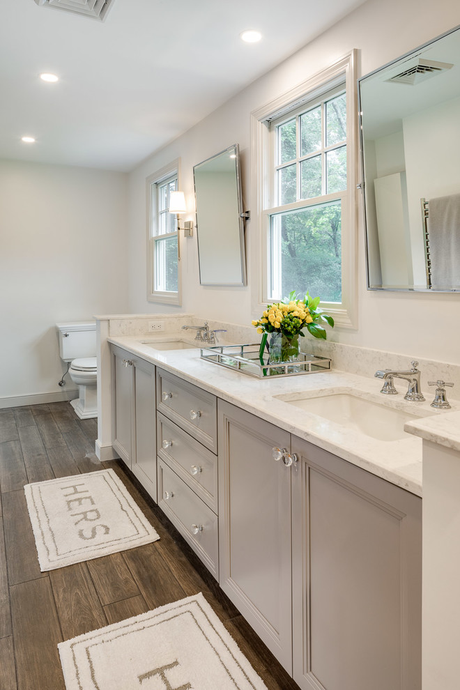 This is an example of a classic ensuite bathroom in Boston with recessed-panel cabinets, grey cabinets, a two-piece toilet, white walls, medium hardwood flooring, a submerged sink, brown floors and white worktops.
