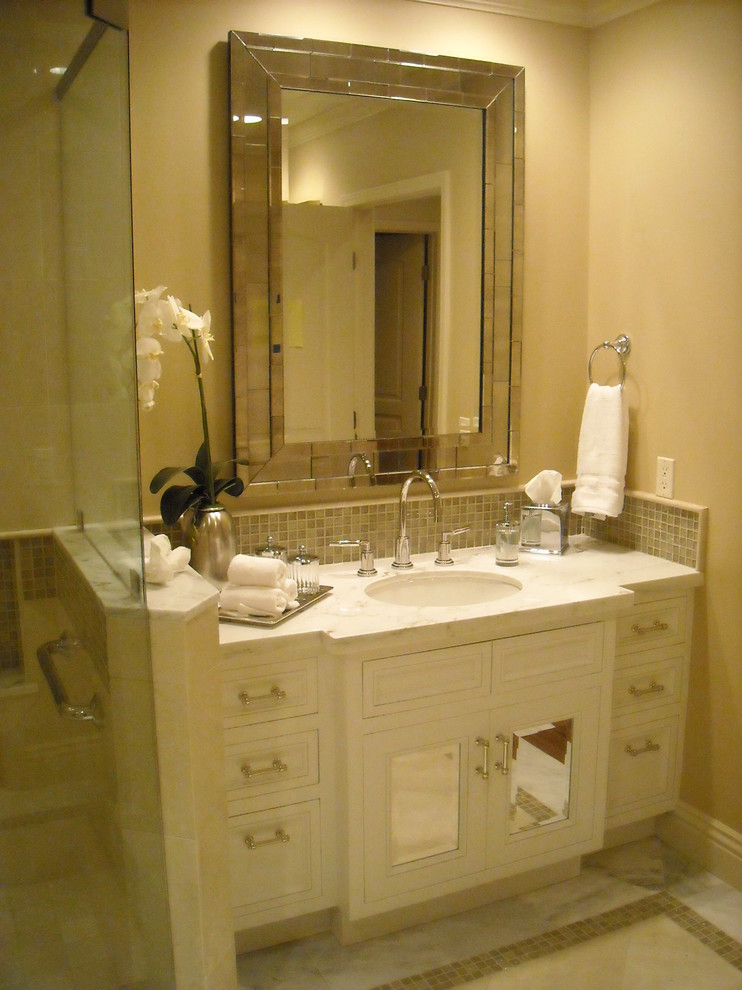 Cette photo montre une salle d'eau chic de taille moyenne avec un lavabo encastré, un placard à porte vitrée, des portes de placard blanches, un plan de toilette en marbre, une baignoire d'angle, une douche d'angle, WC à poser, un carrelage blanc, un carrelage en pâte de verre, un mur beige et un sol en marbre.