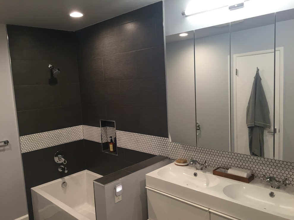Modelo de cuarto de baño contemporáneo de tamaño medio con armarios con paneles lisos, puertas de armario blancas, bañera empotrada, combinación de ducha y bañera, sanitario de dos piezas, baldosas y/o azulejos grises, paredes grises y lavabo integrado