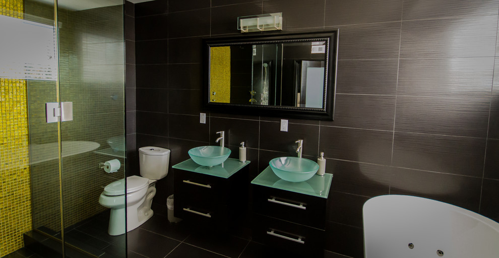 Inspiration för stora moderna en-suite badrum, med släta luckor, svarta skåp, ett fristående badkar, en dusch i en alkov, grå kakel, grå väggar, klinkergolv i porslin, ett fristående handfat, bänkskiva i glas, svart golv och dusch med gångjärnsdörr