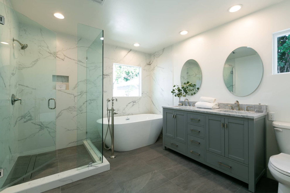 Идея дизайна: большая главная ванная комната в современном стиле с фасадами с утопленной филенкой, серыми фасадами, отдельно стоящей ванной, угловым душем, унитазом-моноблоком, белой плиткой, мраморной плиткой, белыми стенами, полом из керамической плитки, врезной раковиной, мраморной столешницей, серым полом, душем с распашными дверями, серой столешницей, тумбой под две раковины и напольной тумбой