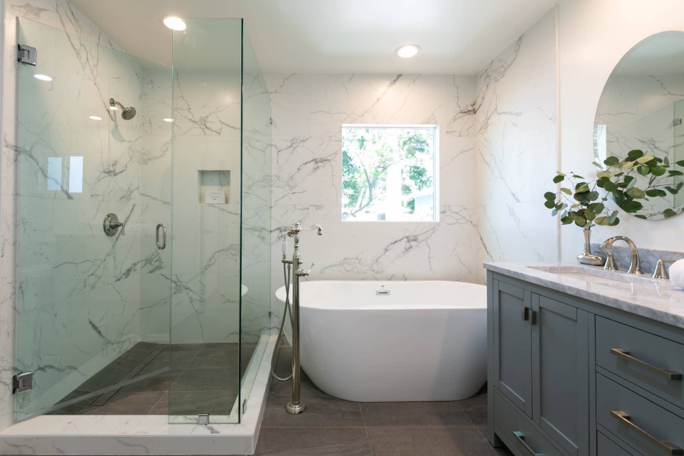 На фото: большая главная ванная комната в современном стиле с фасадами с утопленной филенкой, серыми фасадами, отдельно стоящей ванной, угловым душем, унитазом-моноблоком, белой плиткой, мраморной плиткой, белыми стенами, полом из керамической плитки, врезной раковиной, мраморной столешницей, серым полом, душем с распашными дверями, серой столешницей, тумбой под две раковины и напольной тумбой