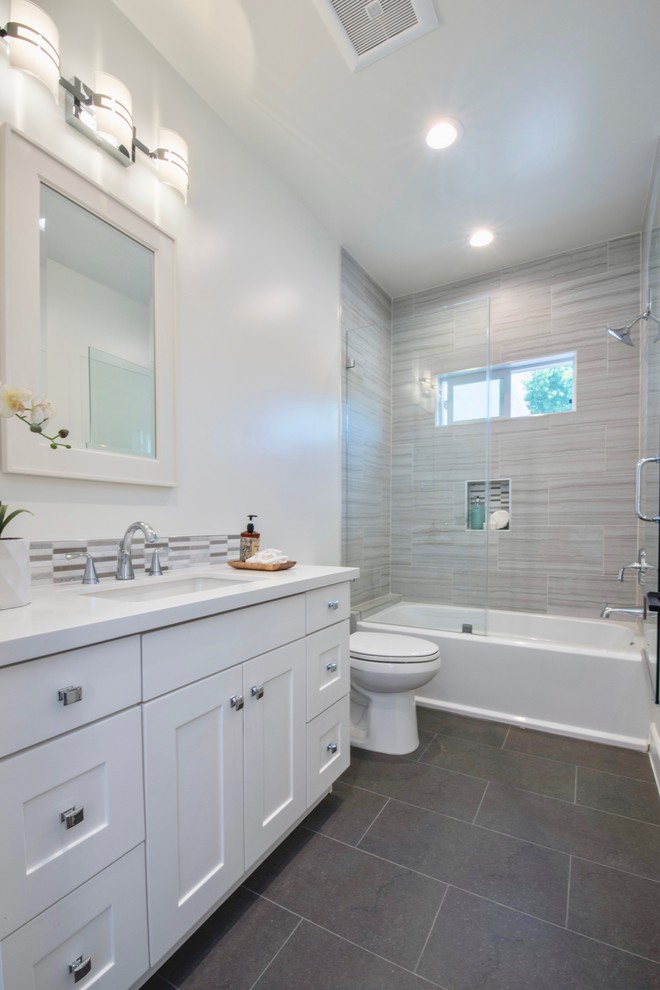 Inspiration for a mid-sized transitional 3/4 gray tile and ceramic tile gray floor bathroom remodel in Los Angeles with shaker cabinets, white cabinets, white walls, a drop-in sink, a hinged shower door and white countertops