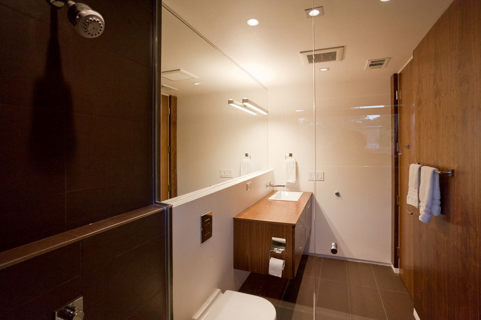 Photo of a medium sized modern ensuite bathroom in Sacramento with a built-in sink, flat-panel cabinets, dark wood cabinets, wooden worktops, a built-in bath, a shower/bath combination, a wall mounted toilet, brown tiles, porcelain tiles, white walls and porcelain flooring.