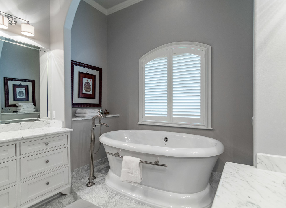 На фото: большая главная ванная комната в классическом стиле с фасадами с утопленной филенкой, белыми фасадами, отдельно стоящей ванной, мраморным полом, врезной раковиной и мраморной столешницей с