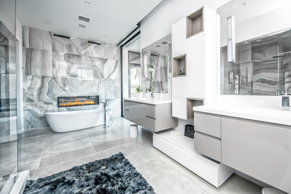 Источник вдохновения для домашнего уюта: главная ванная комната в современном стиле с плоскими фасадами, серыми фасадами, отдельно стоящей ванной, серой плиткой, серыми стенами, монолитной раковиной, серым полом, белой столешницей и зеркалом с подсветкой