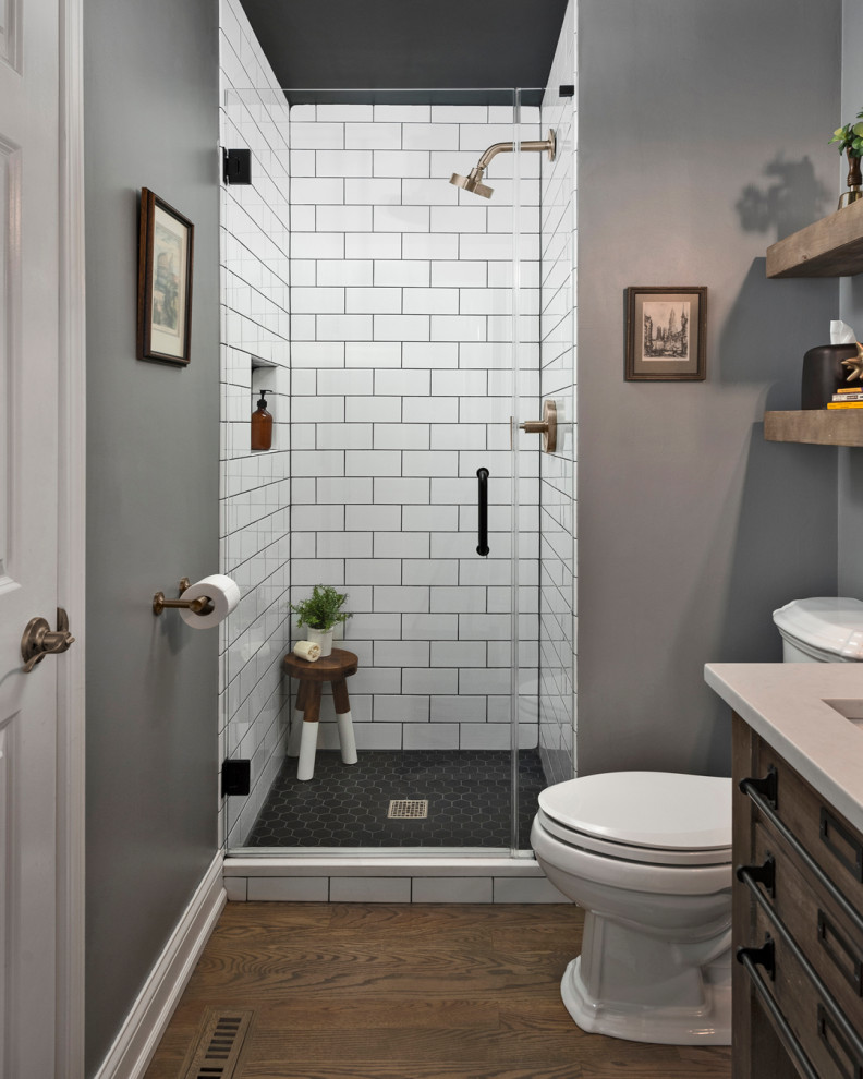 Medium sized traditional shower room bathroom in Chicago with a two-piece toilet, white tiles, ceramic tiles, porcelain flooring, a submerged sink, engineered stone worktops, a hinged door, grey worktops, a single sink, a freestanding vanity unit, dark wood cabinets, an alcove shower, grey walls and brown floors.