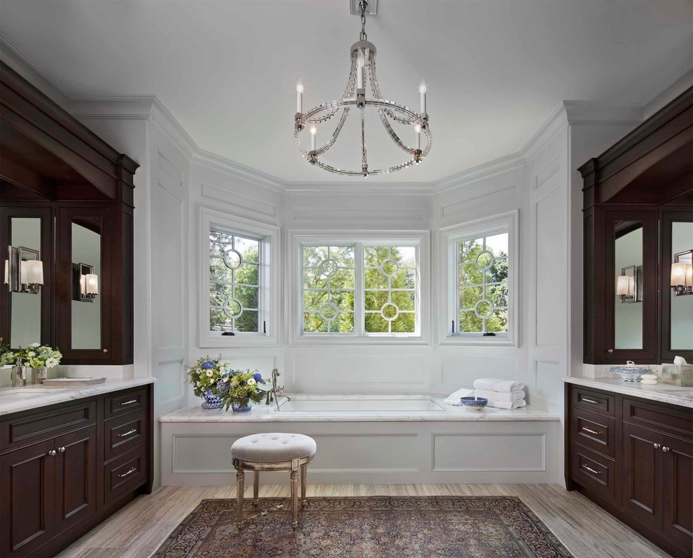 Photo of a classic ensuite bathroom in Detroit with beaded cabinets, medium wood cabinets, a built-in bath, grey tiles, travertine tiles, grey walls, marble worktops, a submerged sink and multi-coloured floors.