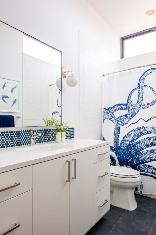 На фото: ванная комната среднего размера в стиле модернизм с плоскими фасадами, белыми фасадами, ванной в нише, душем над ванной, раздельным унитазом, синей плиткой, плиткой мозаикой, белыми стенами, полом из керамогранита, душевой кабиной, врезной раковиной, столешницей из искусственного кварца, черным полом, шторкой для ванной и белой столешницей