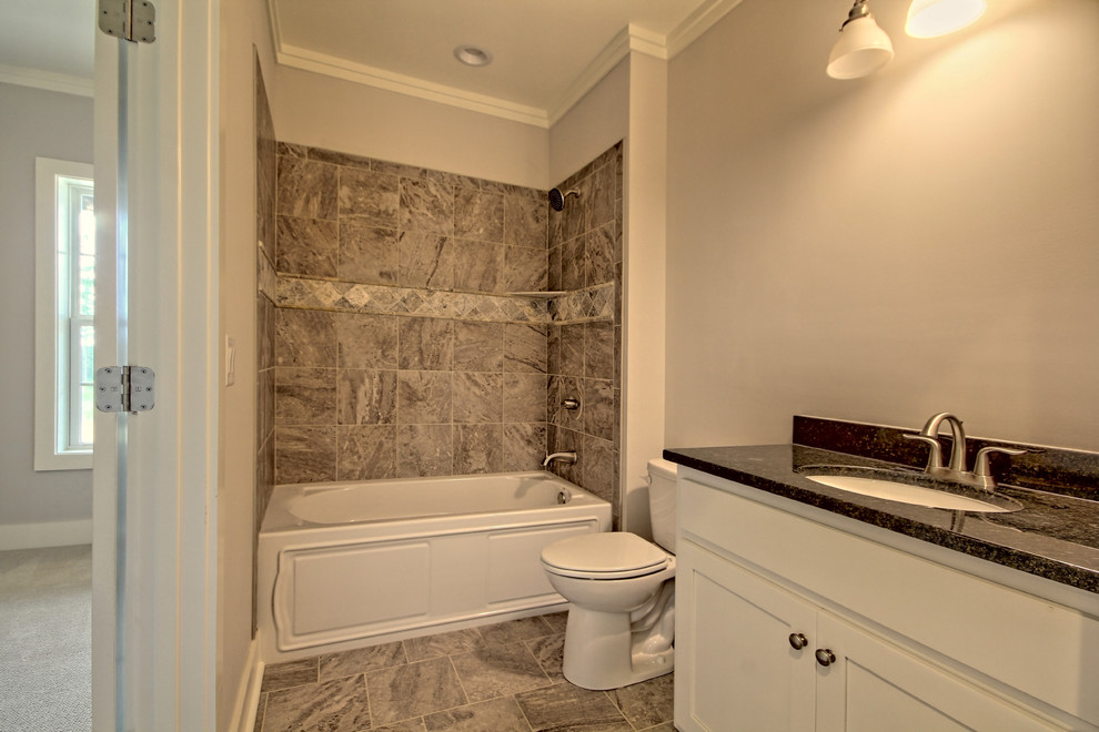 Exempel på ett mellanstort amerikanskt badrum, med luckor med infälld panel, vita skåp, ett badkar i en alkov, en dusch i en alkov, en toalettstol med separat cisternkåpa, grå kakel, stenkakel, grå väggar, klinkergolv i keramik, ett undermonterad handfat och granitbänkskiva