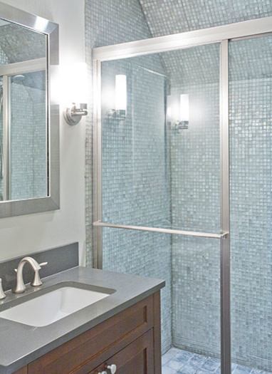 Traditional bathroom in New York with a built-in sink, recessed-panel cabinets, dark wood cabinets, an alcove shower, blue tiles, glass tiles and white walls.
