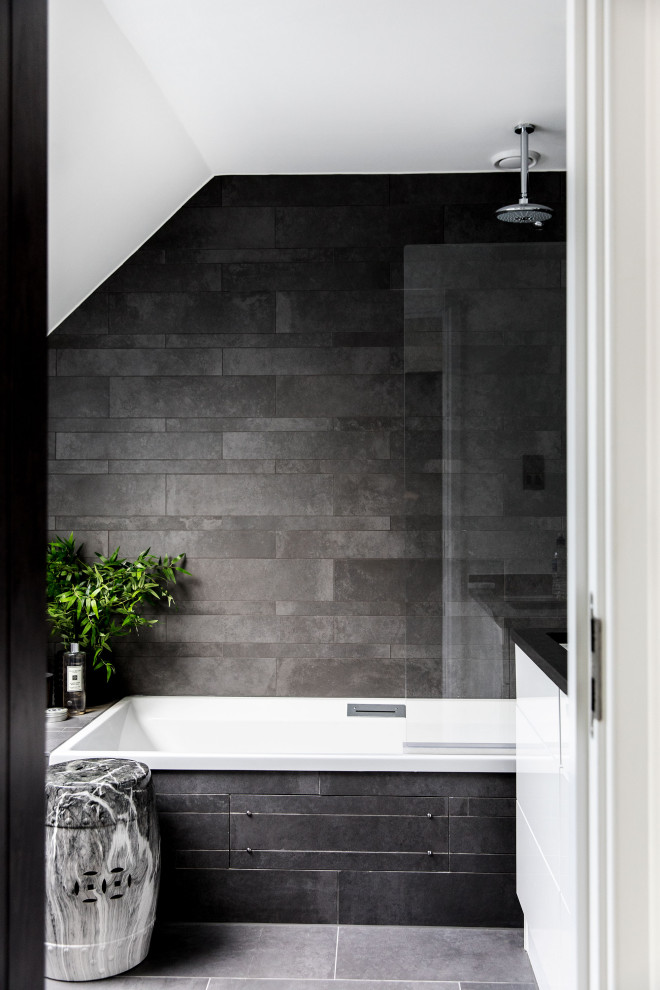 Idee per una stanza da bagno con doccia minimal di medie dimensioni con ante lisce, ante bianche, vasca da incasso, vasca/doccia, piastrelle grigie, pareti grigie, pavimento con piastrelle in ceramica, lavabo sottopiano, top in granito, pavimento grigio e top nero