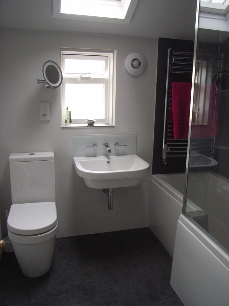 Bild på ett litet funkis badrum för barn, med ett väggmonterat handfat, ett platsbyggt badkar, en dusch/badkar-kombination, en toalettstol med separat cisternkåpa, grå kakel, porslinskakel, grå väggar och linoleumgolv