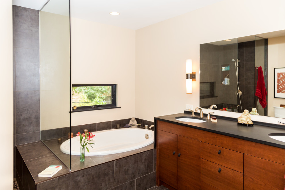 This is an example of a medium sized contemporary ensuite bathroom in Minneapolis with flat-panel cabinets, dark wood cabinets, a built-in bath, a walk-in shower, a two-piece toilet, grey tiles, ceramic tiles, beige walls, ceramic flooring, a submerged sink and solid surface worktops.