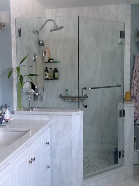 Exemple d'une salle de bain principale chic de taille moyenne avec un placard avec porte à panneau surélevé, des portes de placard blanches, une douche d'angle, un carrelage gris, un carrelage blanc, des dalles de pierre, un mur gris, un lavabo encastré, un plan de toilette en surface solide et une cabine de douche à porte battante.