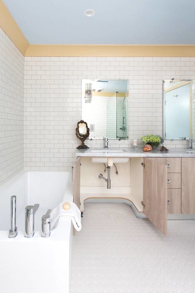 Modern inredning av ett badrum, med ett undermonterad handfat, släta luckor, beige skåp, marmorbänkskiva, ett hörnbadkar, en kantlös dusch, en toalettstol med hel cisternkåpa, vit kakel och keramikplattor