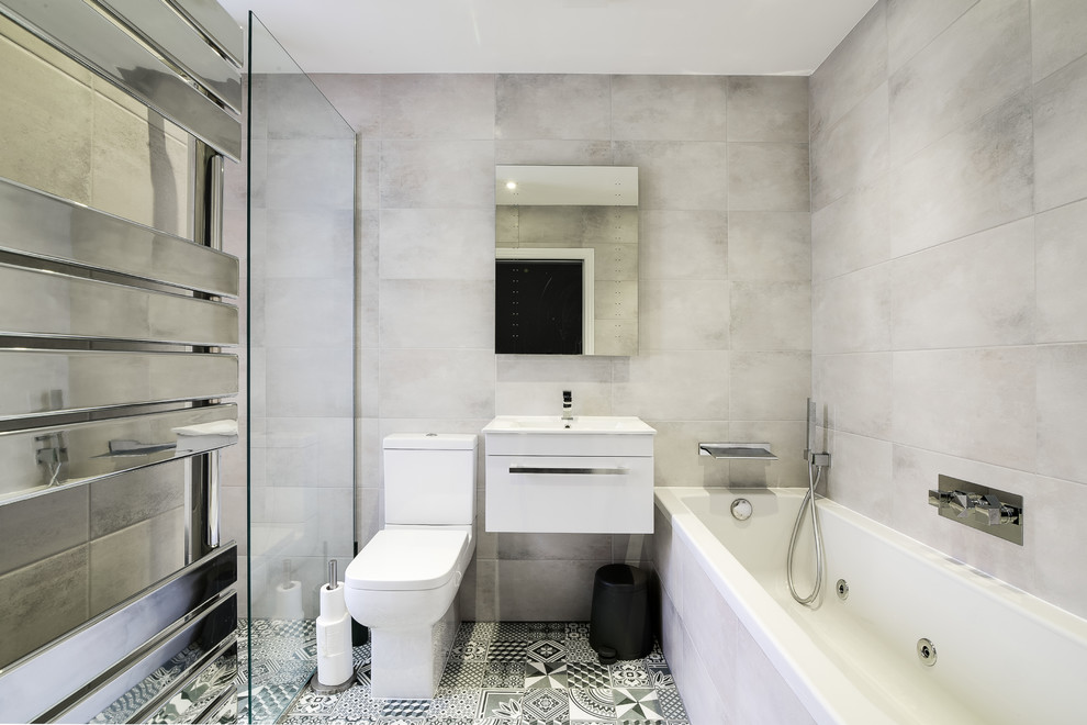 ロンドンにある中くらいなコンテンポラリースタイルのおしゃれな浴室 (フラットパネル扉のキャビネット、白いキャビネット、ドロップイン型浴槽、洗い場付きシャワー、一体型トイレ	、グレーの壁、壁付け型シンク、黒い床) の写真