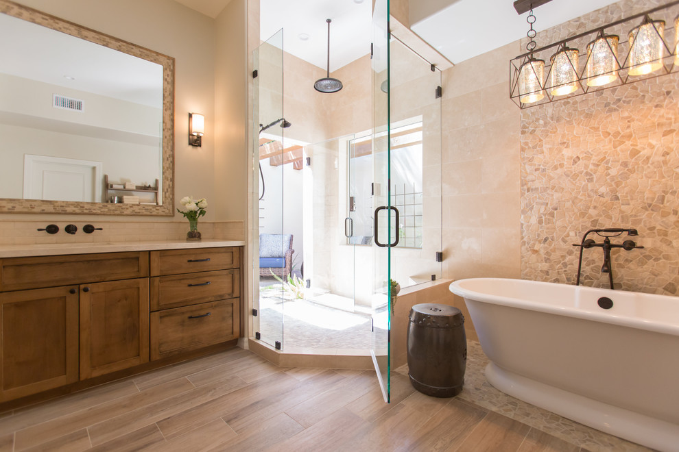 Design ideas for a medium sized mediterranean ensuite bathroom in Phoenix with shaker cabinets, medium wood cabinets, a freestanding bath, a one-piece toilet, beige tiles, travertine tiles, beige walls, porcelain flooring, a submerged sink, marble worktops, beige floors and a hinged door.