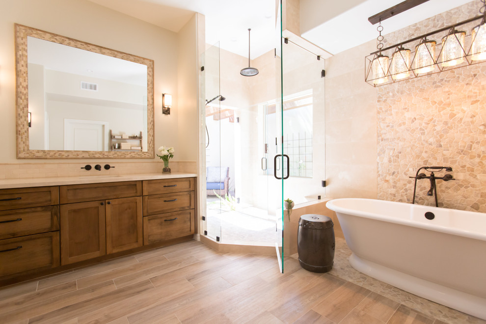Example of a mid-sized tuscan master beige tile and travertine tile porcelain tile and beige floor freestanding bathtub design in Phoenix with shaker cabinets, medium tone wood cabinets, a one-piece toilet, beige walls, an undermount sink, marble countertops and a hinged shower door