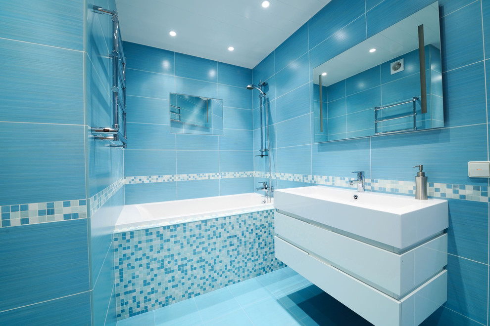 Modelo de cuarto de baño minimalista con lavabo suspendido, puertas de armario blancas, bañera empotrada, combinación de ducha y bañera, baldosas y/o azulejos azules y suelo azul