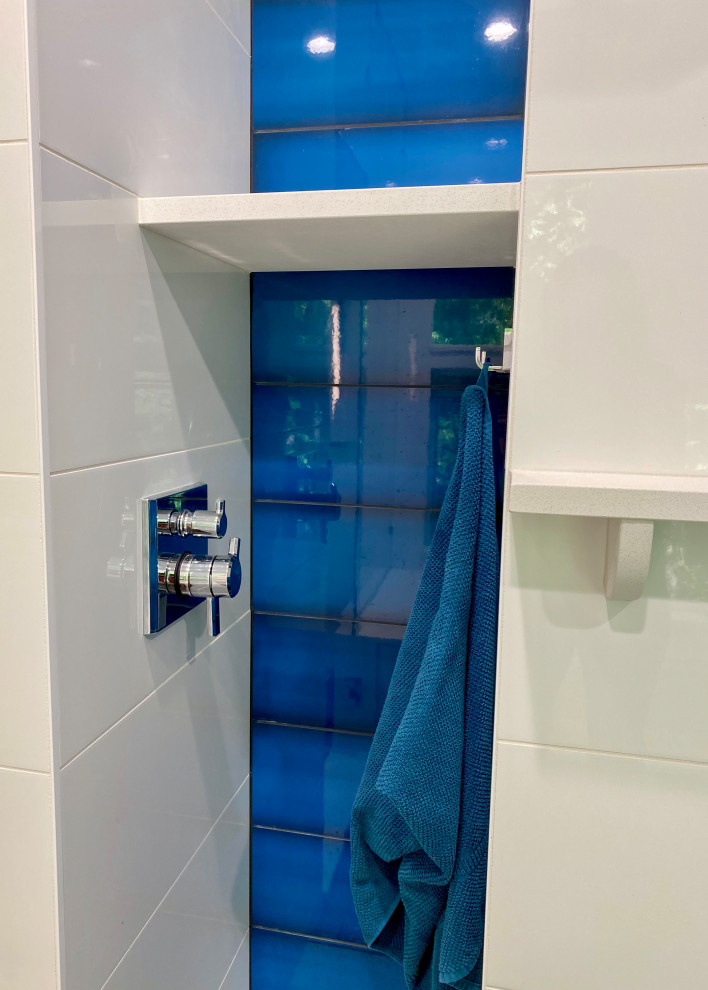Источник вдохновения для домашнего уюта: главная ванная комната среднего размера в современном стиле с плоскими фасадами, серыми фасадами, полновстраиваемой ванной, душем над ванной, унитазом-моноблоком, синей плиткой, стеклянной плиткой, белыми стенами, полом из керамической плитки, врезной раковиной, столешницей из искусственного кварца, серым полом, душем с распашными дверями, белой столешницей, нишей, тумбой под две раковины и подвесной тумбой
