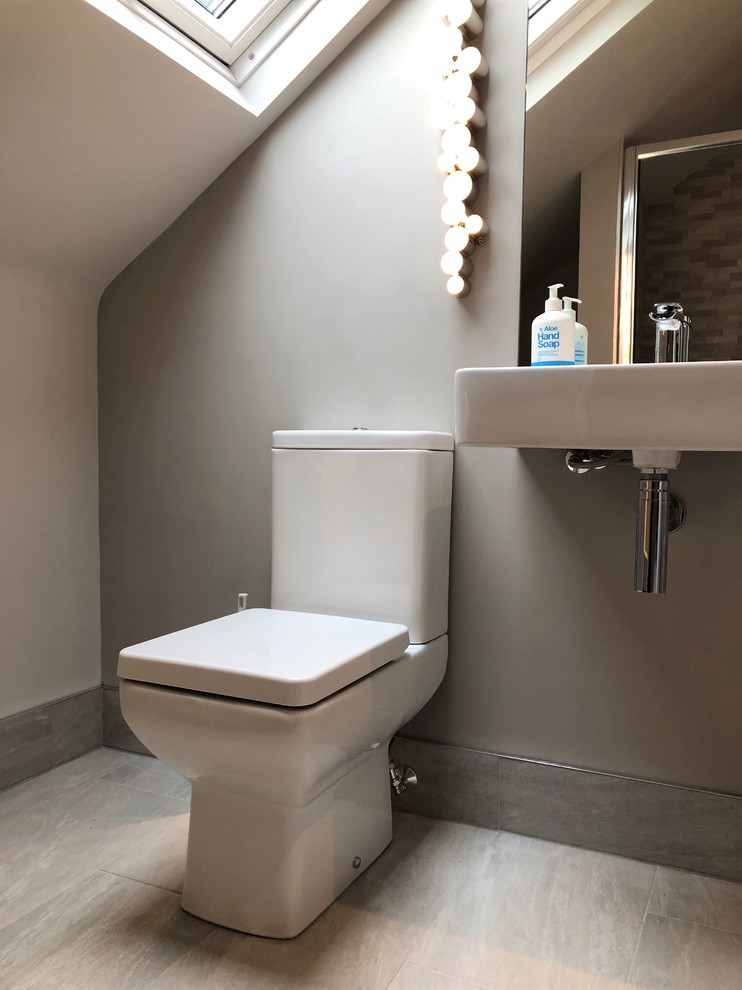 Foto på ett litet funkis toalett, med en toalettstol med separat cisternkåpa, grå kakel, porslinskakel, grå väggar, klinkergolv i porslin, ett väggmonterat handfat och grått golv