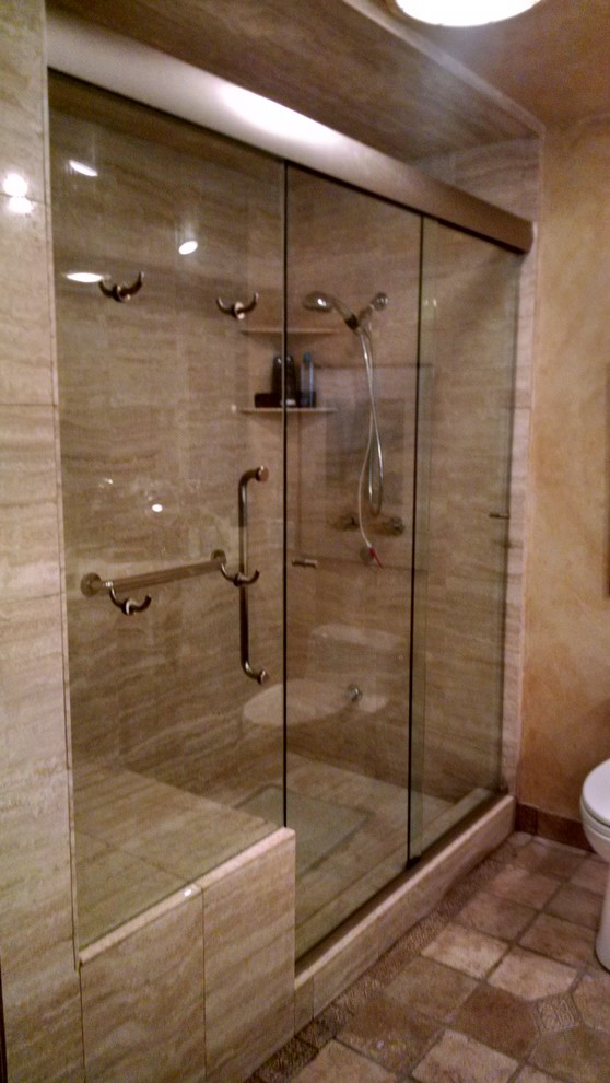 ソルトレイクシティにあるトラディショナルスタイルのおしゃれな浴室 (アルコーブ型シャワー、茶色いタイル、石タイル、茶色い壁、テラコッタタイルの床、マルチカラーの床、開き戸のシャワー) の写真