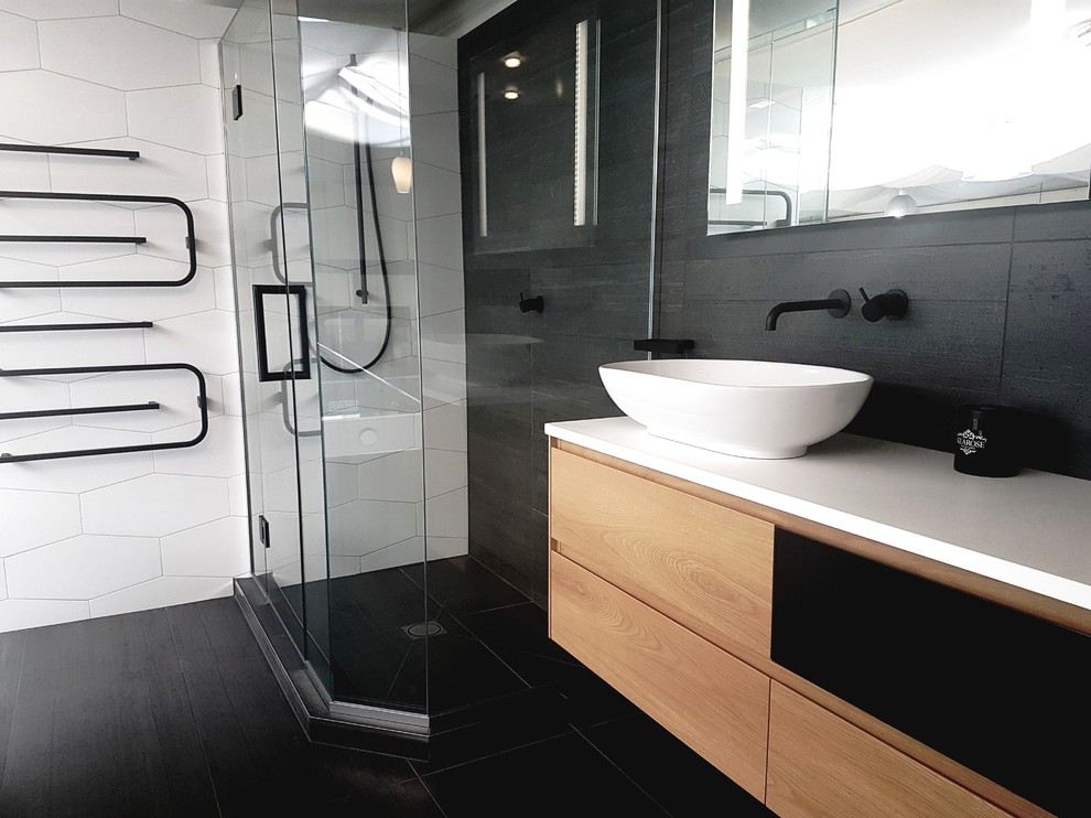Mittelgroßes Modernes Badezimmer mit verzierten Schränken, hellen Holzschränken, Eckdusche, schwarz-weißen Fliesen, Porzellanfliesen, schwarzer Wandfarbe, Porzellan-Bodenfliesen, Aufsatzwaschbecken, Mineralwerkstoff-Waschtisch, schwarzem Boden und Falttür-Duschabtrennung in Auckland