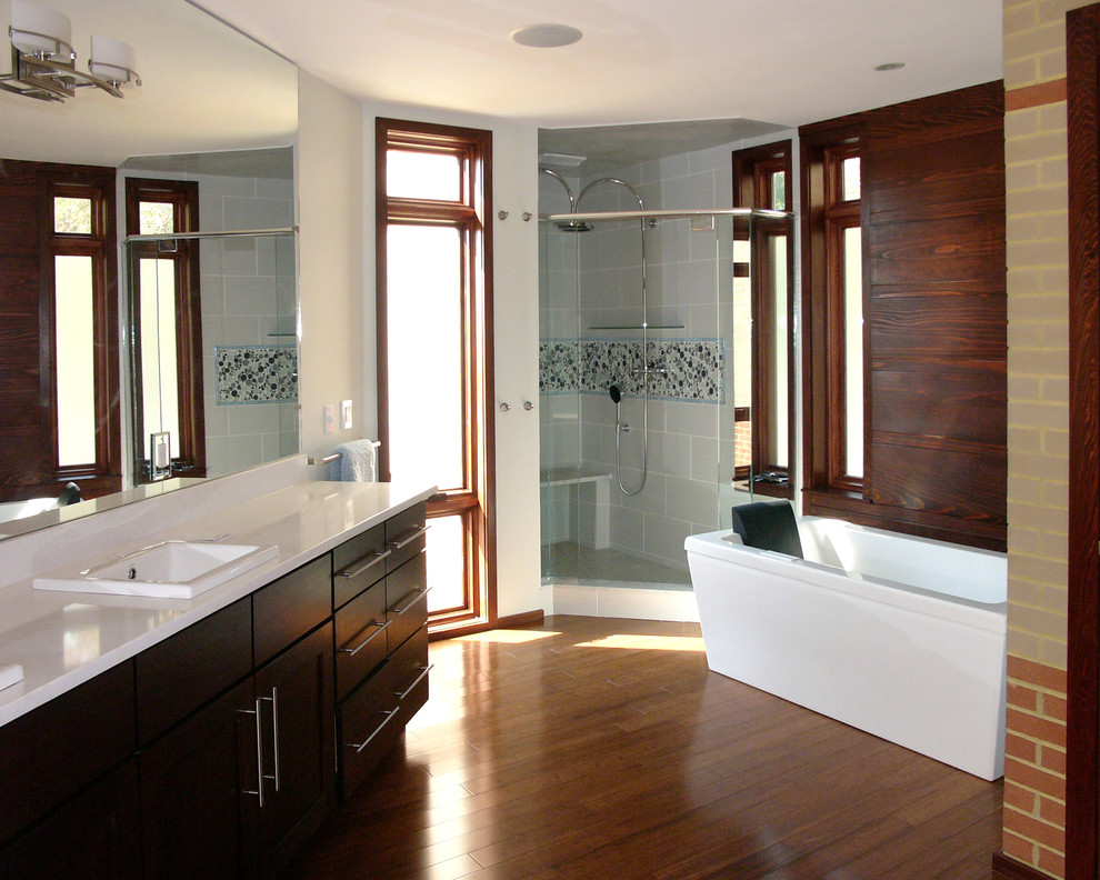 Inredning av ett modernt stort en-suite badrum, med släta luckor, skåp i mörkt trä, ett fristående badkar, en hörndusch, grå kakel, porslinskakel, bruna väggar, mörkt trägolv, ett nedsänkt handfat, bänkskiva i akrylsten, brunt golv och dusch med gångjärnsdörr