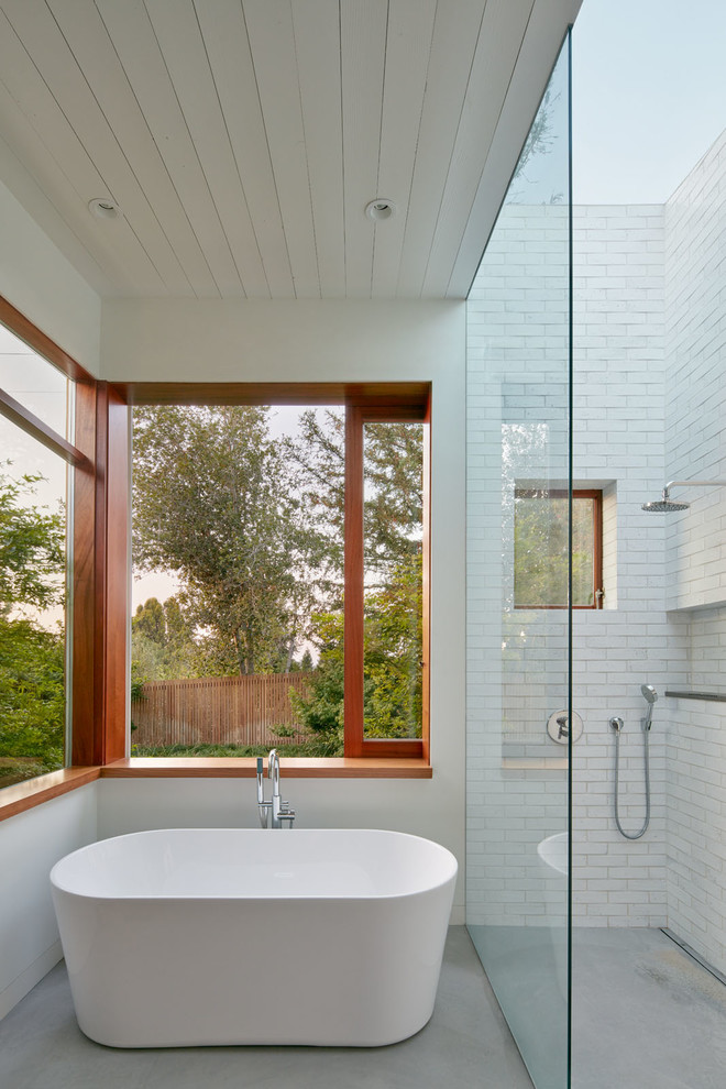 Пример оригинального дизайна: главная ванная комната в современном стиле с отдельно стоящей ванной, душем без бортиков, белой плиткой, белыми стенами, бетонным полом, открытым душем и окном
