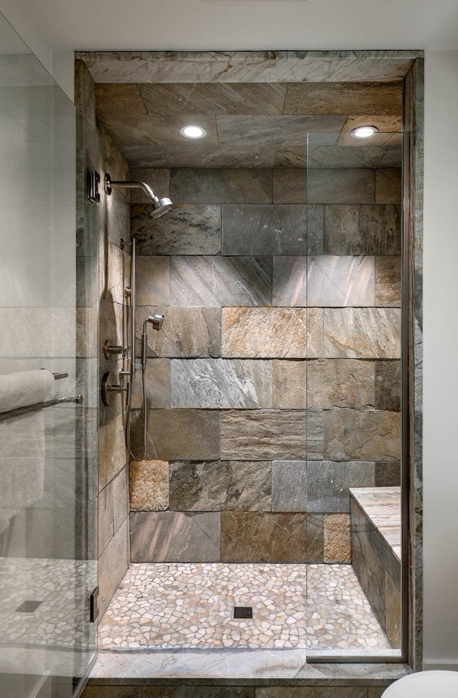 Modelo de cuarto de baño principal de estilo americano con ducha empotrada, baldosas y/o azulejos de piedra, paredes blancas, suelo de baldosas tipo guijarro, suelo gris y ducha con puerta con bisagras