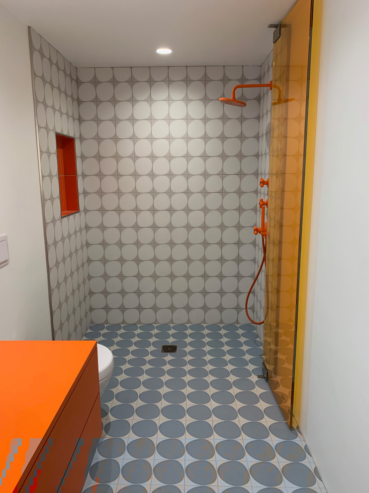Exempel på ett mellanstort modernt orange oranget badrum, med släta luckor, orange skåp, en kantlös dusch, en vägghängd toalettstol, grå kakel, porslinskakel, vita väggar, klinkergolv i porslin, ett fristående handfat, laminatbänkskiva, blått golv och dusch med gångjärnsdörr