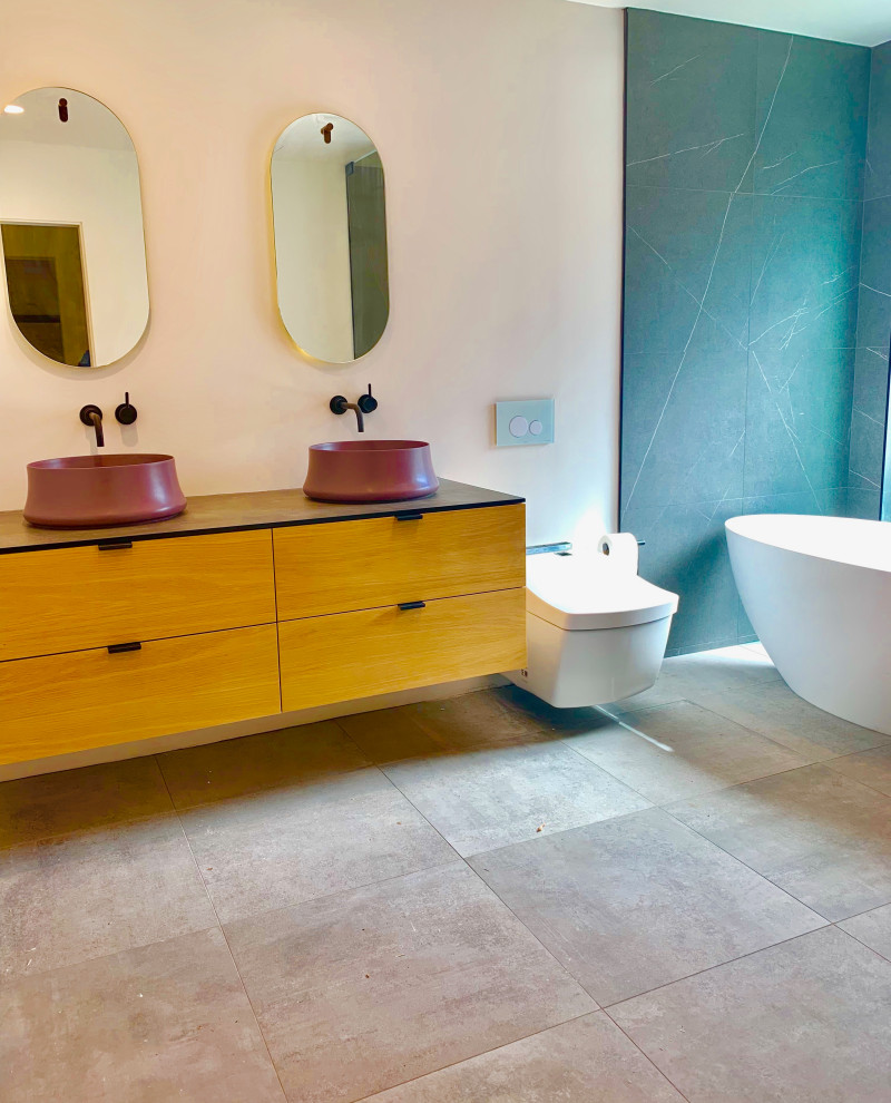 Photo of a large contemporary ensuite bathroom in Los Angeles with purple cabinets, a freestanding bath, a built-in shower, a wall mounted toilet, porcelain flooring, a vessel sink, grey floors, a hinged door, grey worktops, freestanding cabinets, grey tiles, porcelain tiles, pink walls and tiled worktops.