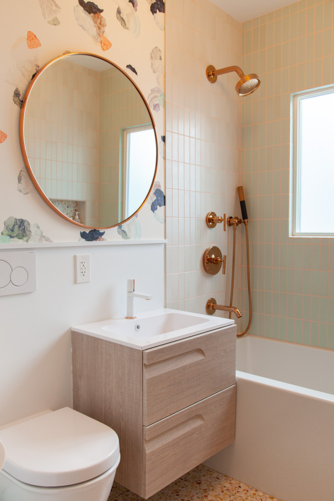 На фото: ванная комната в скандинавском стиле с плоскими фасадами, светлыми деревянными фасадами, ванной в нише, душем над ванной, инсталляцией, зеленой плиткой, разноцветными стенами, полом из терраццо, монолитной раковиной, разноцветным полом и белой столешницей с