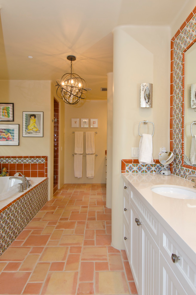 フェニックスにある高級な中くらいなサンタフェスタイルのおしゃれな浴室 (アンダーカウンター洗面器、落し込みパネル扉のキャビネット、白いキャビネット、ライムストーンの洗面台、ドロップイン型浴槽、アルコーブ型シャワー、ベージュの壁、テラコッタタイルの床、マルチカラーのタイル) の写真