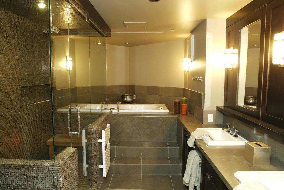 Inredning av ett en-suite badrum, med ett nedsänkt handfat, släta luckor, skåp i mörkt trä, bänkskiva i kvartsit, ett badkar i en alkov, en dubbeldusch, brun kakel, mosaik, beige väggar och klinkergolv i porslin