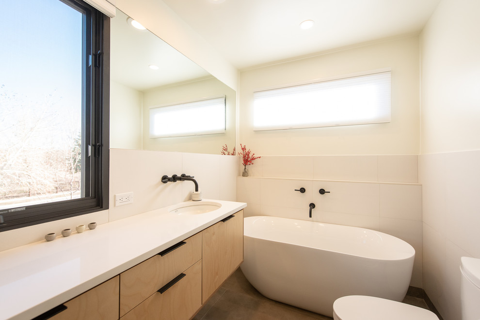 Ispirazione per una stanza da bagno minimal con ante in legno chiaro, top bianco, ante lisce, vasca freestanding, pareti beige, lavabo sottopiano e pavimento grigio