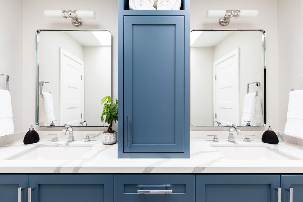 Cette image montre une salle de bain traditionnelle avec un placard à porte shaker, des portes de placard bleues, un mur beige, un lavabo encastré et un plan de toilette blanc.