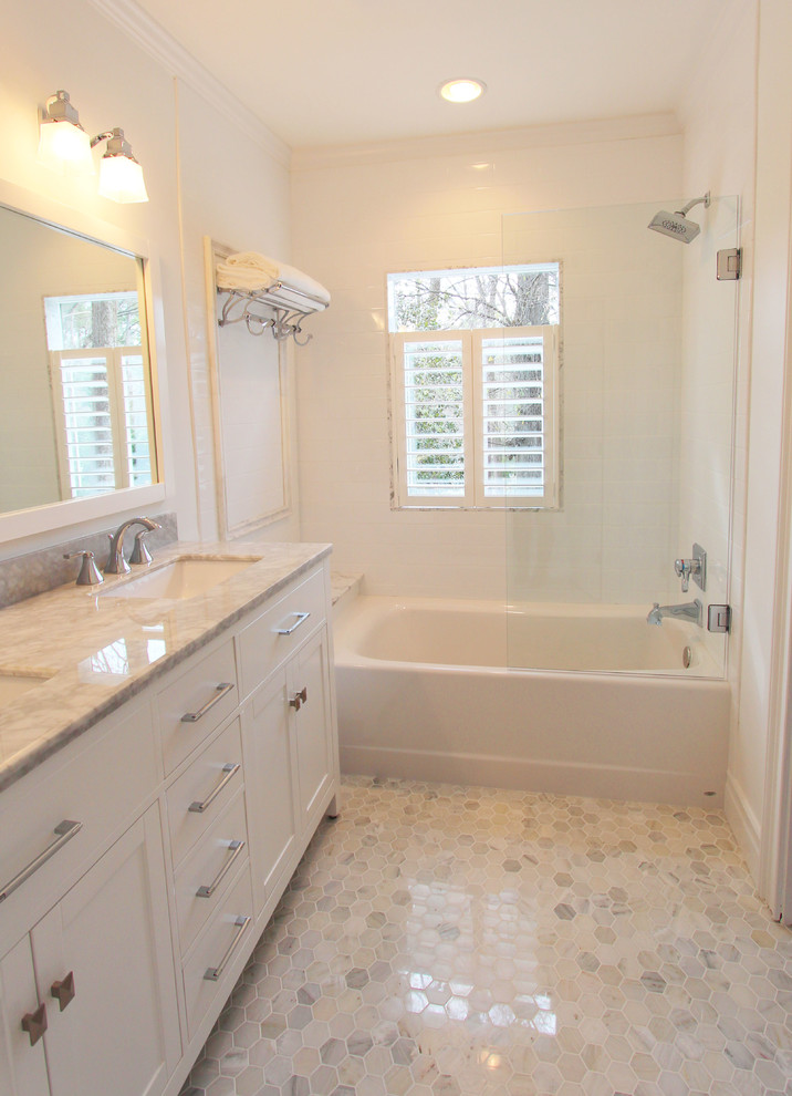 Inredning av ett klassiskt litet badrum, med ett undermonterad handfat, släta luckor, vita skåp, marmorbänkskiva, ett badkar i en alkov, en dusch/badkar-kombination, en toalettstol med separat cisternkåpa, vit kakel, keramikplattor, vita väggar och marmorgolv