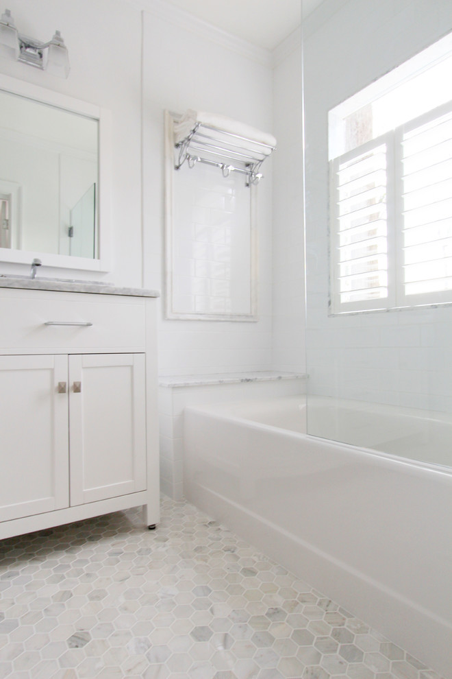 Klassisk inredning av ett litet badrum, med ett undermonterad handfat, vita skåp, marmorbänkskiva, ett badkar i en alkov, en dusch/badkar-kombination, en toalettstol med separat cisternkåpa, vit kakel, keramikplattor, vita väggar, marmorgolv och skåp i shakerstil