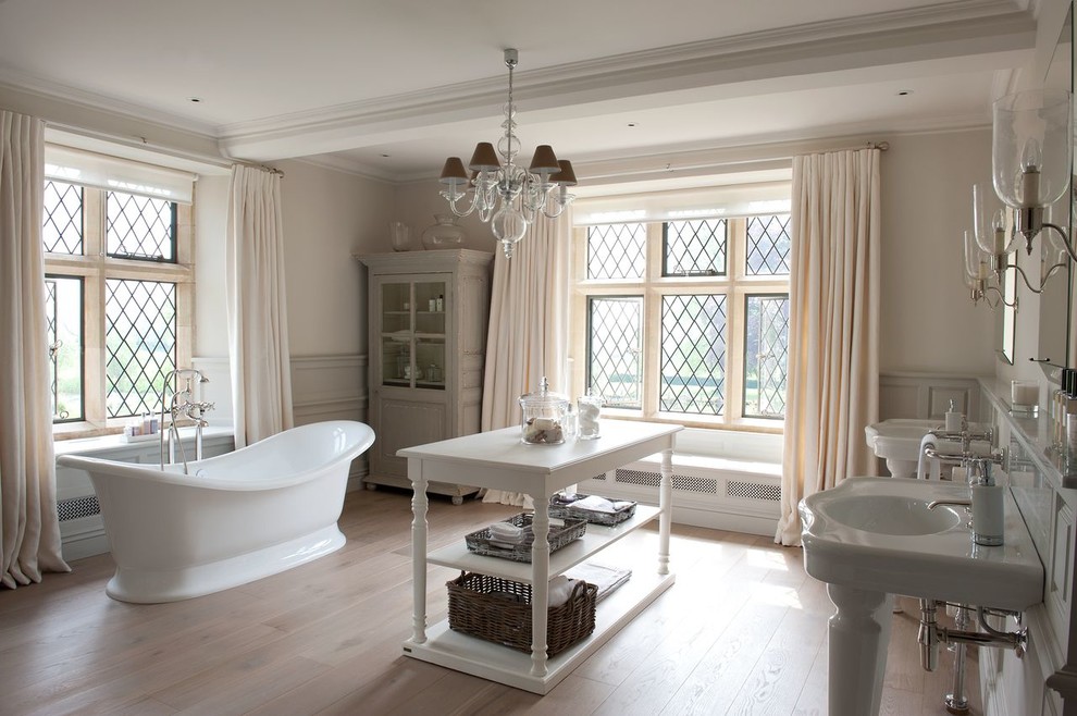 Immagine di una stanza da bagno padronale country con lavabo a consolle, top in marmo, vasca freestanding, pareti bianche e parquet chiaro