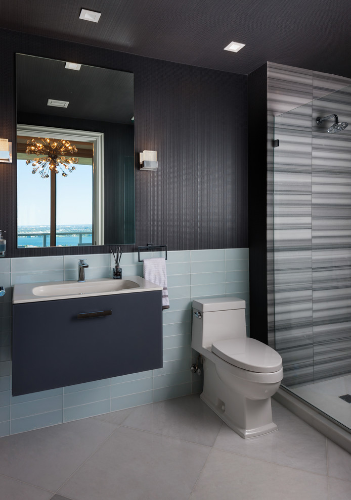 Cette image montre une salle de bain design avec un placard à porte plane, des portes de placard bleues, WC à poser, un carrelage bleu, un carrelage en pâte de verre, un mur noir, un plan vasque, un sol gris, un plan de toilette en quartz modifié et un plan de toilette beige.