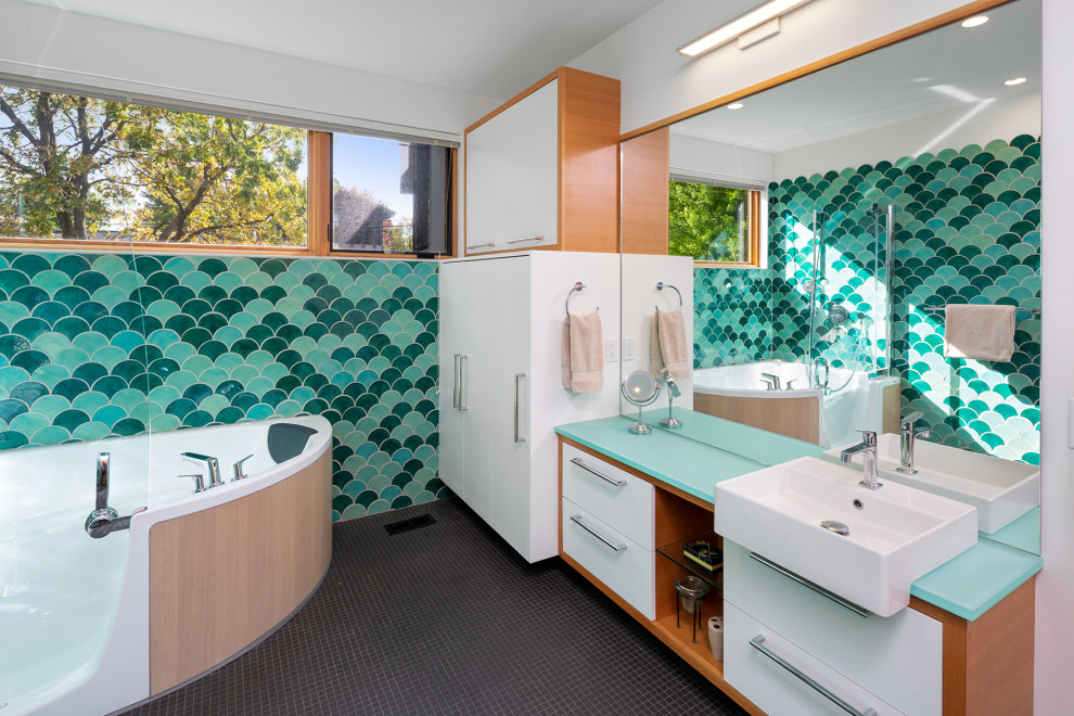 Идея дизайна: главная ванная комната в современном стиле с плоскими фасадами, белыми фасадами, угловой ванной, душем над ванной, зеленой плиткой, разноцветной плиткой, белыми стенами, полом из мозаичной плитки, настольной раковиной, стеклянной столешницей, черным полом, душем с распашными дверями и синей столешницей