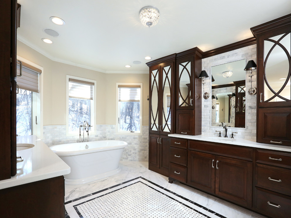 Modelo de cuarto de baño principal tradicional extra grande con puertas de armario de madera en tonos medios, bañera exenta y baldosas y/o azulejos grises