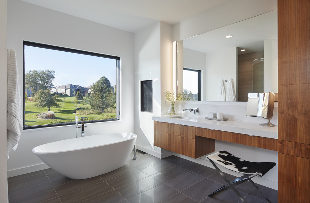 Cette photo montre une salle de bain principale moderne en bois brun avec un placard à porte plane, une baignoire indépendante, un mur blanc, un lavabo encastré et un sol gris.