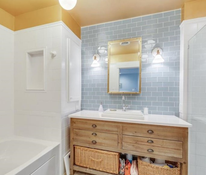 Photo of a medium sized urban ensuite bathroom in New York with freestanding cabinets, distressed cabinets, an alcove bath, an alcove shower, a two-piece toilet, blue tiles, glass tiles, yellow walls, porcelain flooring, a built-in sink, engineered stone worktops, multi-coloured floors, a hinged door and white worktops.