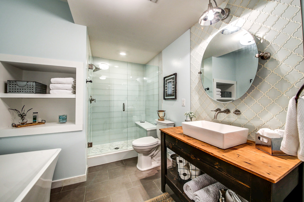 Inredning av ett klassiskt mellanstort brun brunt en-suite badrum, med skåp i slitet trä, ett fristående badkar, en dusch i en alkov, en toalettstol med separat cisternkåpa, glaskakel, blå väggar, ett fristående handfat, träbänkskiva, blå kakel, klinkergolv i porslin, grått golv, dusch med gångjärnsdörr och öppna hyllor