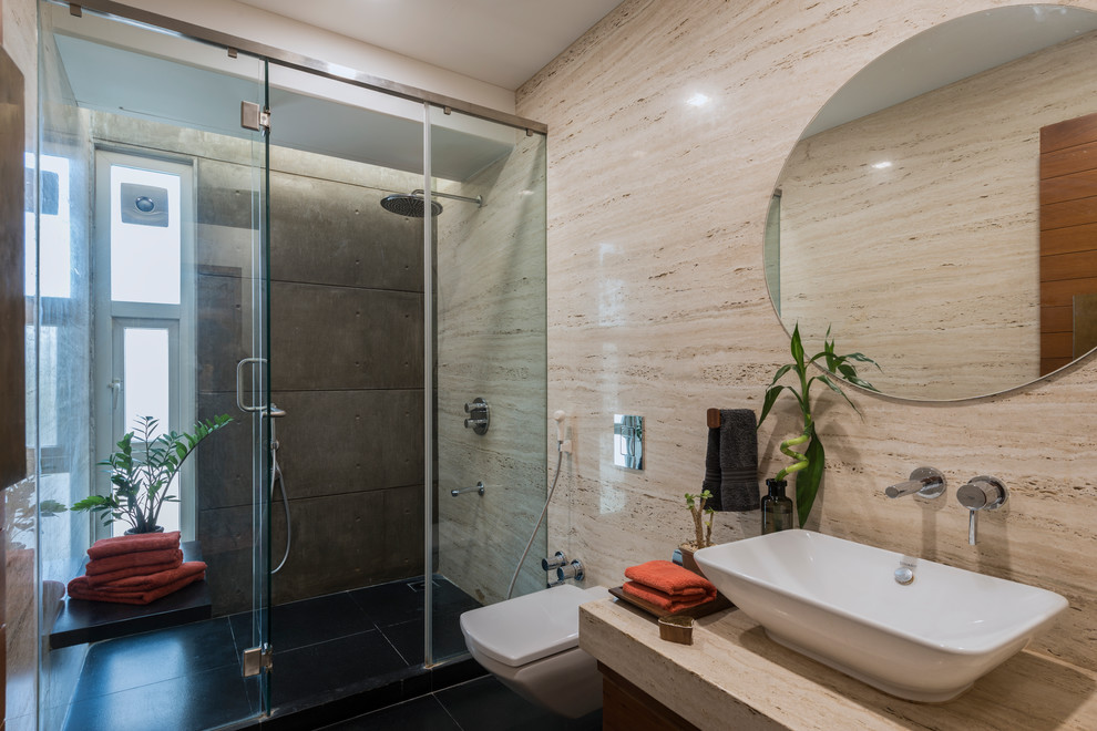 Réalisation d'une salle de bain design avec WC suspendus, un carrelage beige, des dalles de pierre, un mur beige, sol en béton ciré, une vasque, un sol noir et une cabine de douche à porte battante.