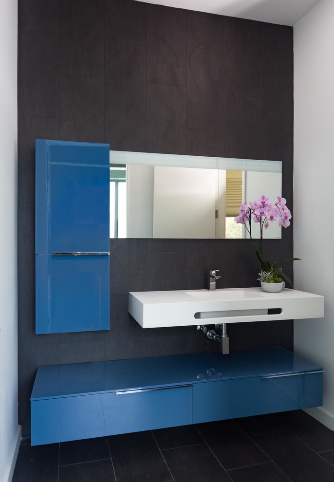 Идея дизайна: ванная комната в современном стиле с плоскими фасадами, синими фасадами, черной плиткой, керамогранитной плиткой, черными стенами, полом из керамогранита, черным полом, белой столешницей и монолитной раковиной